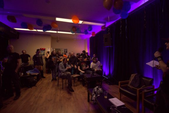 A vibrant gathering with purple lighting and colorful decorations, focused on an audience.