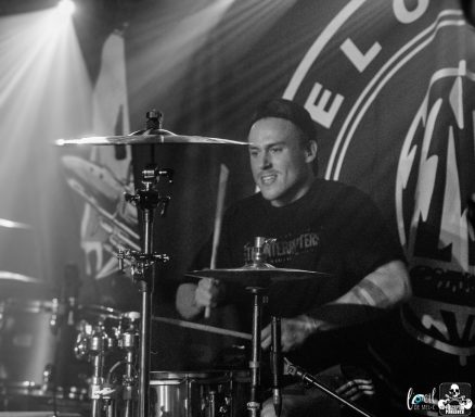 A drummer performing on stage with dramatic lighting in the background.