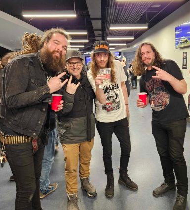 Four people posing together, holding red cups, in an indoor space.