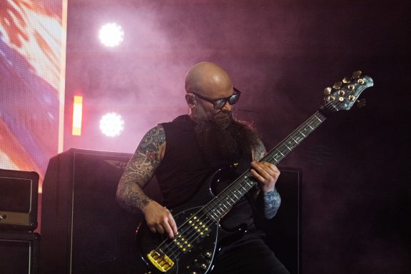 +LIVE+ - Centre Videotron Bald musician with a beard playing a bass guitar on stage with smoke and lights.