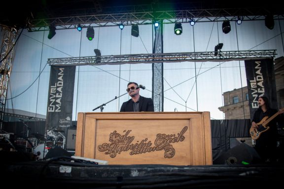 A musician performing on stage at a festival, playing a large keyboard.
