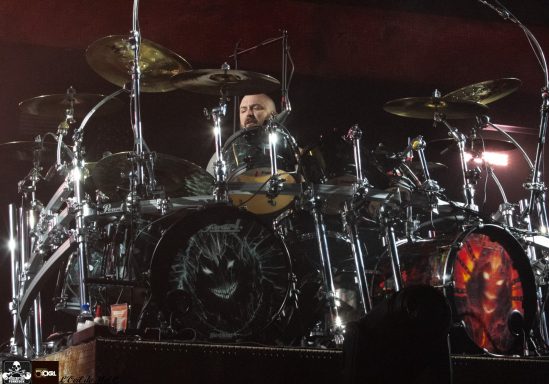 Drummer performing on stage with a complex drum set and vibrant lighting.