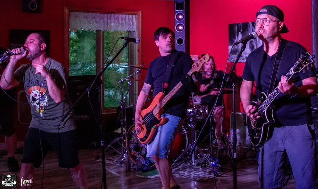 Four musicians perform on stage, playing instruments and singing in a vibrant, colorful setting.