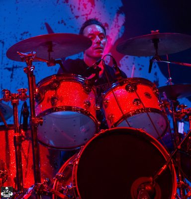 Drummer performing on stage with vibrant lighting.