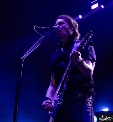 Musician passionately performing on stage with a guitar and microphone.