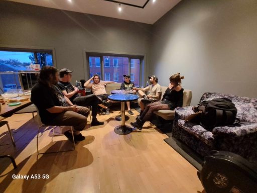 Group of six people seated in a modern living room, engaged in conversation.
