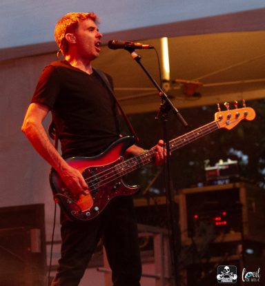 Musician playing a bass guitar and singing on stage during a performance.