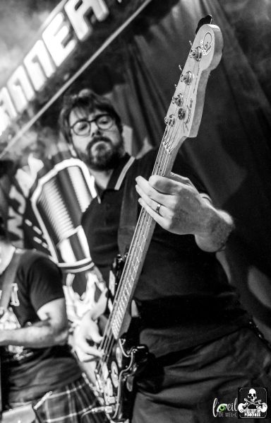A musician plays bass guitar on stage, surrounded by smoke and a vibrant backdrop.
