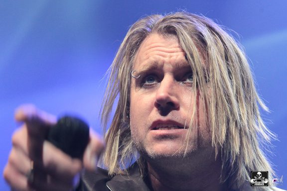 A musician passionately points while performing on stage with dramatic lighting.