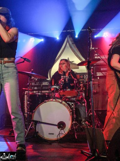 Mvll Crimes - La Source de la Martinière A band performs on stage, with a female vocalist and a drummer visible.