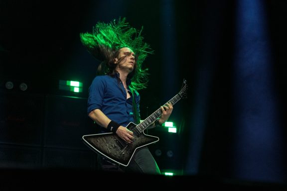 Musician playing electric guitar with long hair flowing in the air.
