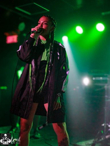 A performer singing on stage with green lighting and a confident stance.