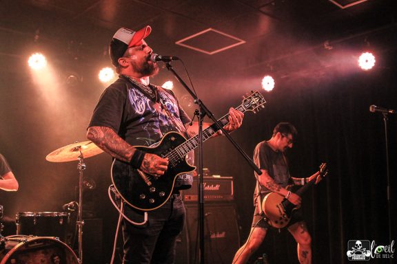 Musicians performing on stage with guitars under colorful stage lights.