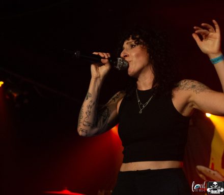Singer performing on stage with a microphone, wearing a black crop top and displaying tattoos.