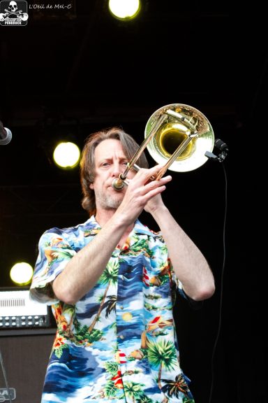Man in a floral shirt playing the trombone on stage.