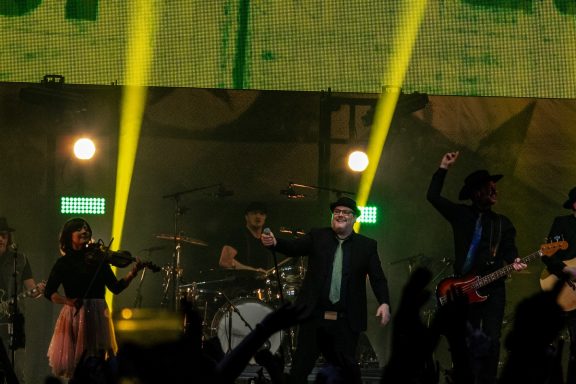 A lively concert scene with performers on stage and bright lights.