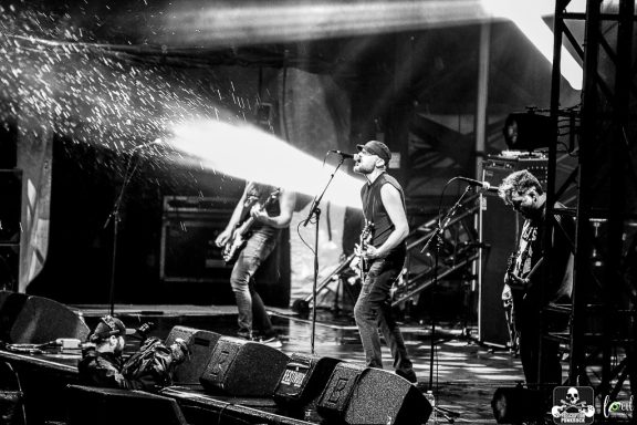 Band performing on stage with dramatic lighting and spray effects in black and white.