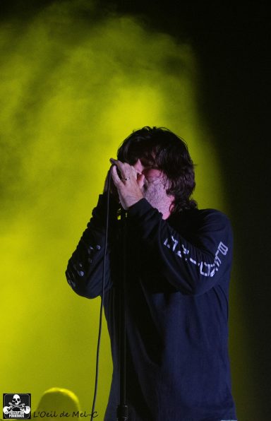 Musician performing on stage with hands covering their face, illuminated by yellow light.