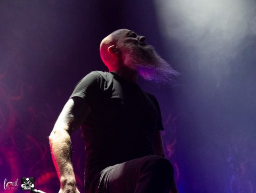A musician with a beard performs on stage, surrounded by dramatic lighting.