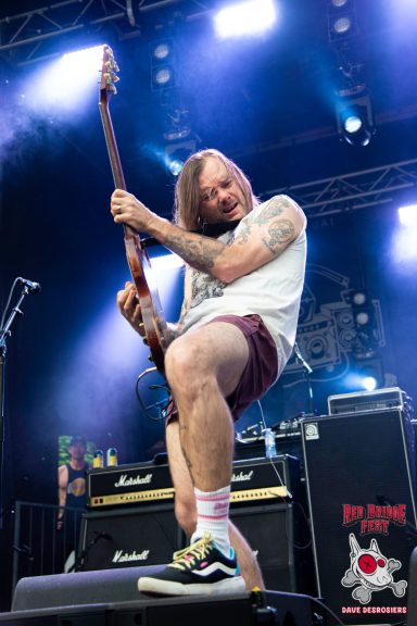 Musician playing guitar on stage, showcasing energetic performance and vibrant lighting.