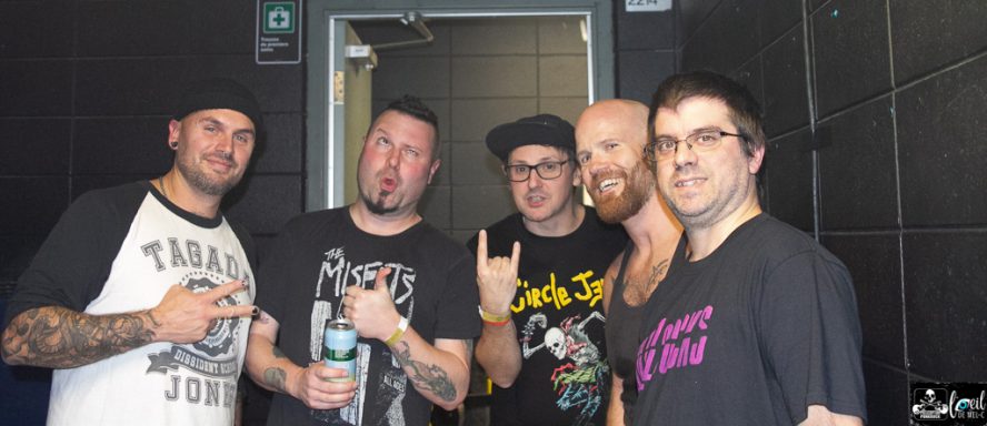 Five men pose together, smiling, in a backstage setting.