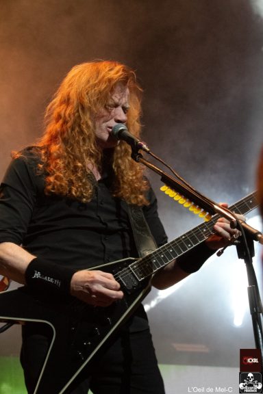Musician with long red hair playing electric guitar on stage.