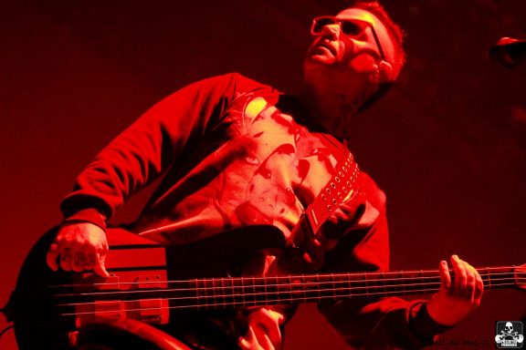 Musician playing a bass guitar on stage with dramatic red lighting.