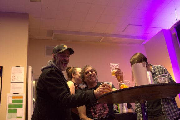 Group of people at a bar with drinks, chatting in a lively atmosphere.