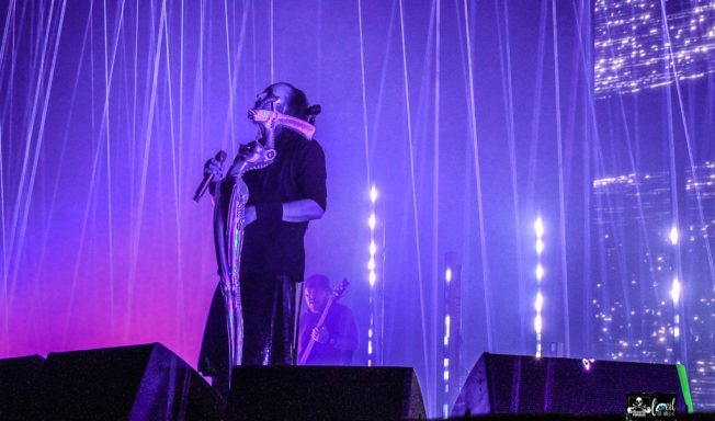 Performer on stage with vibrant lighting and a sheer curtain backdrop.