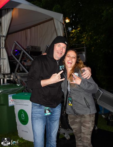 Two people posing together outdoors, smiling and making rock gestures.