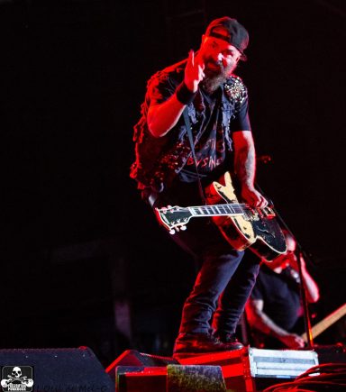 Musician performing on stage, gesturing while playing an electric guitar.