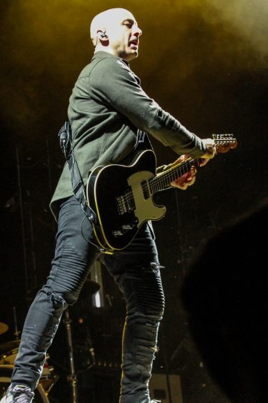 Musician performing on stage, holding a guitar, with dramatic lighting.