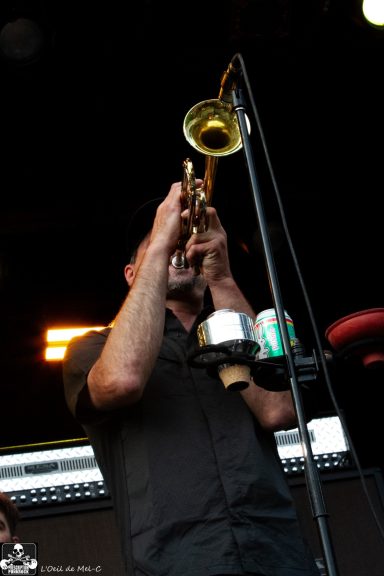 Musician playing a trumpet on stage with a microphone and a can nearby.