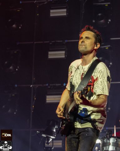 Musician performing on stage, playing guitar with a focused expression.