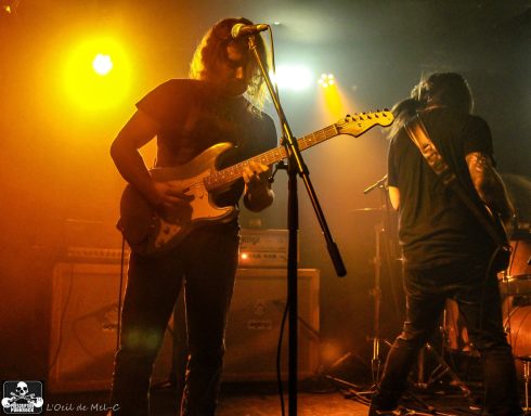 Two musicians performing on stage with electric guitars and dramatic lighting.