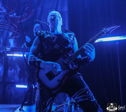 A musician performing on stage, playing an electric guitar with dramatic blue lighting.