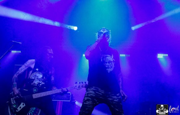 A singer in a dark shirt performs on stage beside a bass guitarist with vibrant lights.