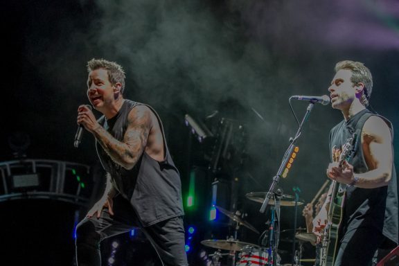 Two male musicians perform on stage, engaging with the crowd and showcasing instruments.