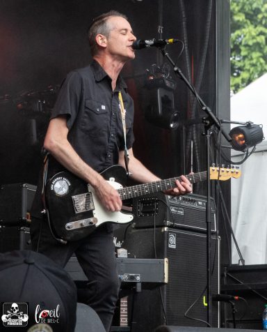 Musician performing on stage, playing guitar and singing into a microphone.