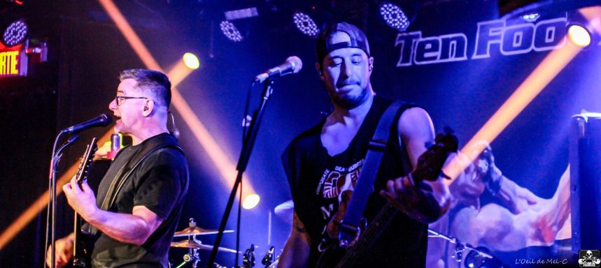 Two musicians perform on stage with instruments, spotlighted by colorful lights.