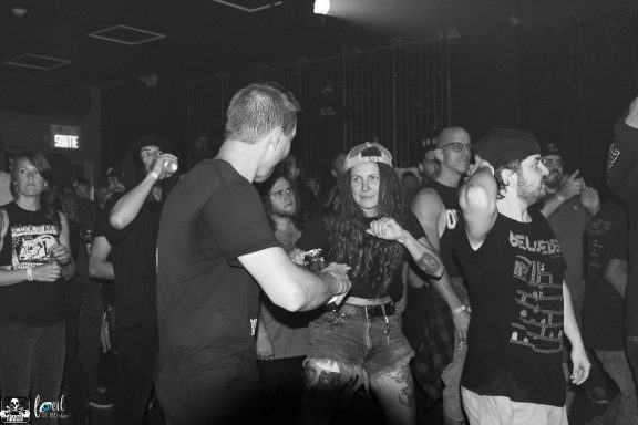 Crowd enjoying a live music performance, dancing and socializing in a dimly lit venue.