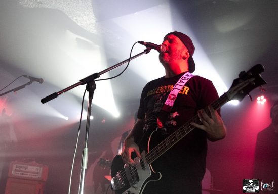 Musician playing guitar and singing on stage with stage lights in the background.