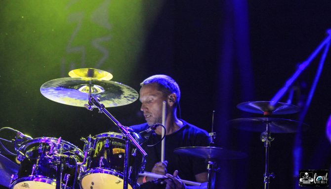 Drummer performing on stage with vibrant lighting.