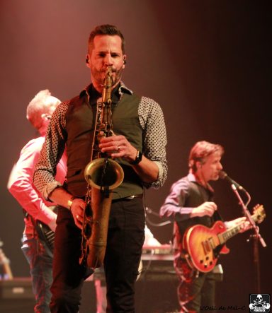 Musicians performing on stage, with a saxophonist in the foreground.