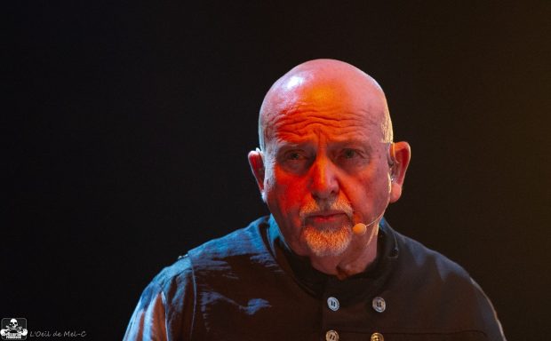 Elderly man with a bald head and serious expression, wearing a dark shirt.