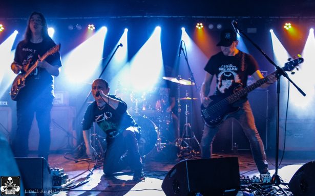 A rock band performs passionately on stage with vibrant blue and purple lighting.
