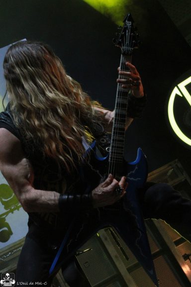 Musician with long hair playing a blue electric guitar on stage.