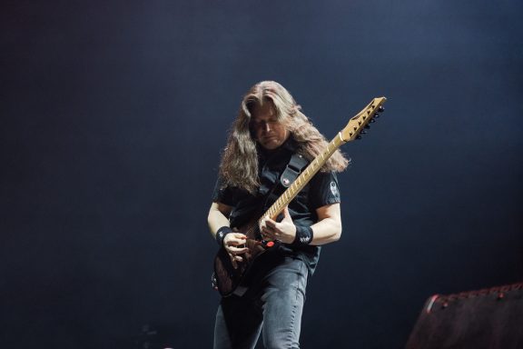 Musician playing electric guitar on stage with dramatic lighting.