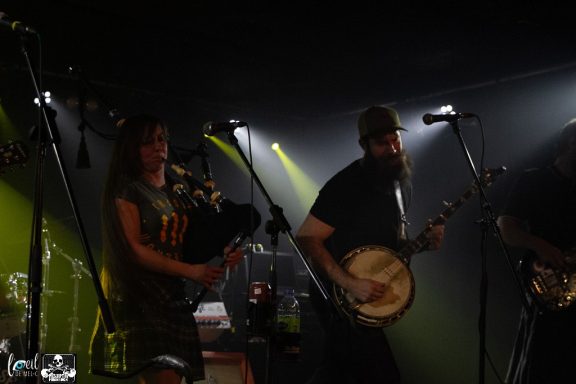 Musicians perform on stage with instruments in a dimly lit venue.