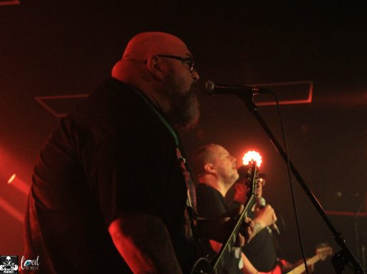 Two musicians performing on stage, focused on their instruments under red lighting.